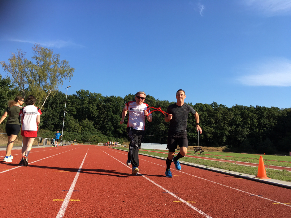 Running Blind-atleet en buddy rennen samen richting finish. Ze zijn met elkaar in contact via een rood lint.