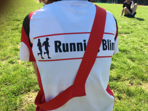 Atleet met Running Blind-shirt op de rug gefotografeerd. Het lintje waarmee atleet en buddy contact houden heeft ze nu even over haar schouder hangen